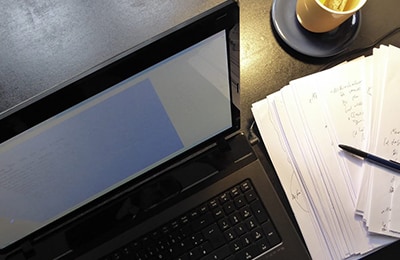 Ein Laptop, eine Tasse Tee und beschriebene Blätter