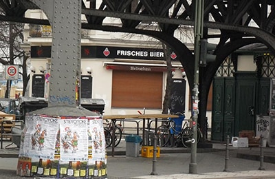 Industrielle Brücke, unter der Tische und Bänke stehen. Direkt dahinter eine Kneipe.