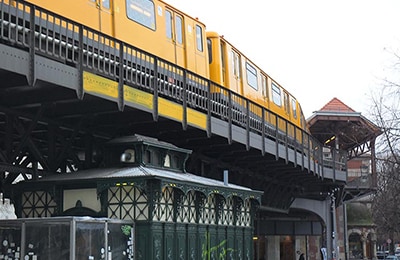 Gelbe Bahn, die auf einer dunkelgrauen Brücke ein paar Meter über einer Straße fährt.