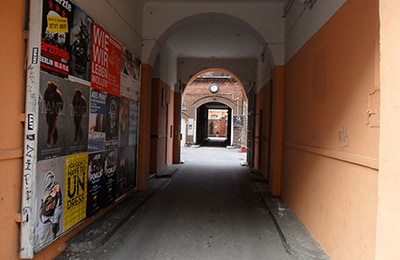 Durchgang, dessen linke Seite mit Postern vollgeklebt und ansonsten orange gestrichen ist.