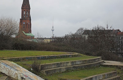 Bild aus Park in Kreuzkölln mit Steinbänken und Blick auf eine Kirche in der Ferne.